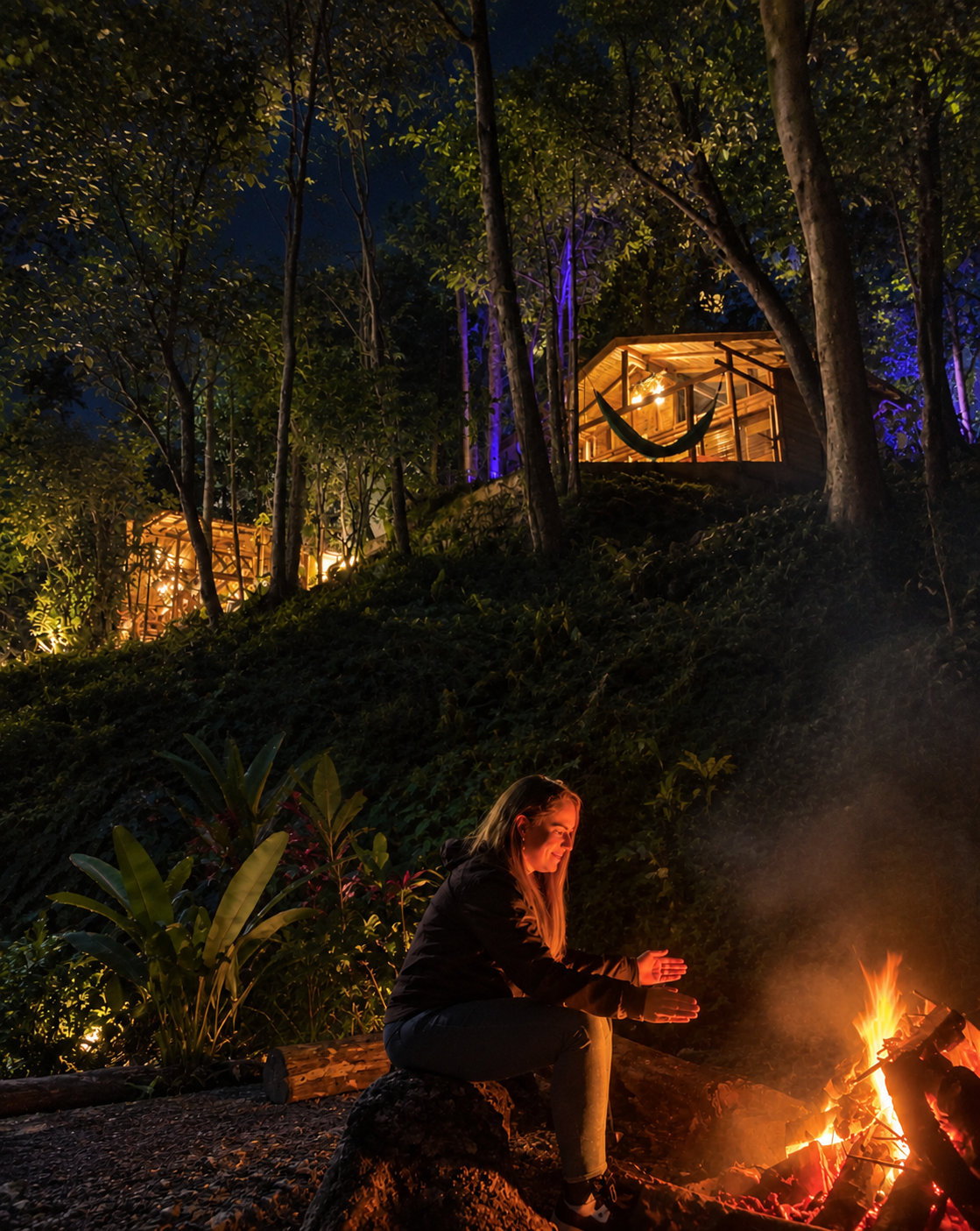 Huésped calentándose junto a la fogata nocturna entre las cabañas iluminadas del bosque